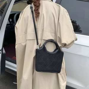 Détail du sac seau noir en daim matelassé montrant la forme trapèze et l'anse en cuir