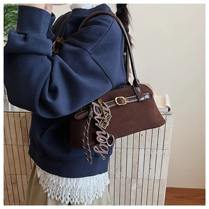 Close-up of matte dark brown underarm bag with a creative boy letter pendant