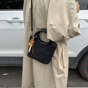 Détail d'un sac à main en daim noir matelassé avec charme en bois et poignée ronde