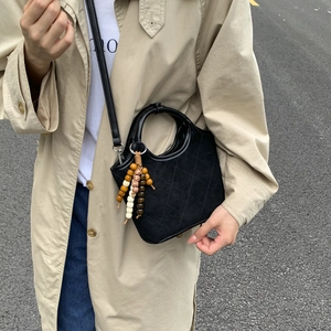 Détail d'un sac seau noir matelassé avec charm en perles de bois et finition en daim