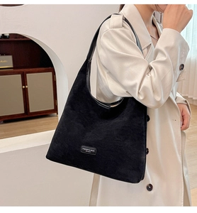Detail of minimalist black suede hobo bag with metal logo on light trench coat