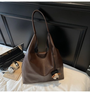 Detail of dark brown faux leather hobo bag with white puppy plush keychain on white bedding