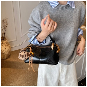 Detail of black glossy leather handbag with gold chain handle and leopard print tassel charm