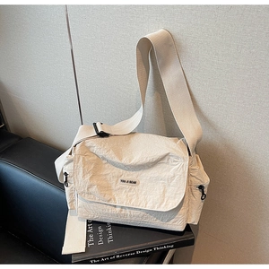 Detail of a creamy white nylon messenger bag with unique pleated texture on a chair