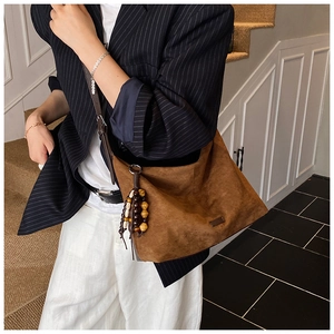 Detail view of large brown suede tote bag with ethnic wooden bead charm and long shoulder strap
