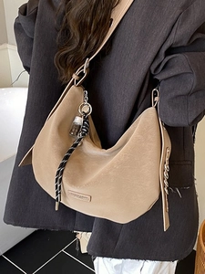 Retro beige crescent tote bag with metal chain strap worn on shoulder with suit
