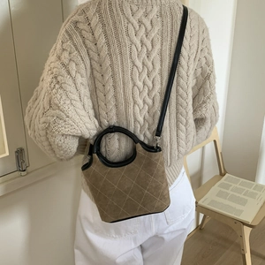 Détail du sac seau en daim matelassé porté avec un pull en maille beige élégant
