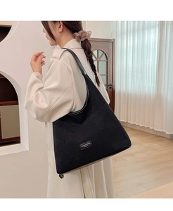 Detailed shot of a black matte tote bag with smooth leather straps and metal brand logo