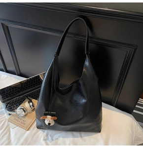 Close-up of black lychee texture hobo bag with a plush dog charm and wide shoulder strap