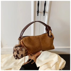 Detail of brown suede handbag featuring a gold chain buckle and leopard print pom-pom charm