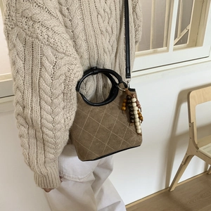 Détail d'un sac seau marron en daim matelassé avec poignées noires et décoration de perles
