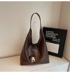 Detail of dark brown faux leather shoulder bag featuring a cute plush puppy pendant charm