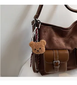 Close-up of brown suede tote with leather pocket, metal lock and cute bear charm