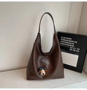 Detail view of large brown hobo bag with pebble texture and cute plush puppy charm