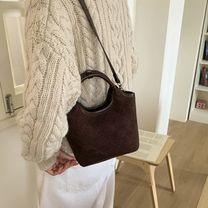 Sac seau matelassé en daim marron porté avec un pull en maille torsadée ivoire