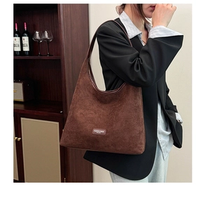 Detail of dark brown suede tote bag featuring a leather logo and premium matte texture