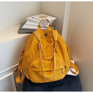 Detail view of a large yellow nylon backpack with multi-pocket design on a chair