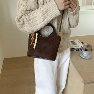 Détail du sac seau en daim marron foncé avec coutures matelassées et breloque en perles
