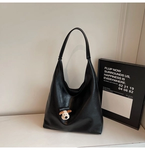 Minimalist black PU leather hobo bag with a cute plush puppy charm on a white surface