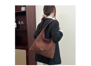 Detail of a dark brown suede hobo bag with a fashion logo tag and minimalist leather strap