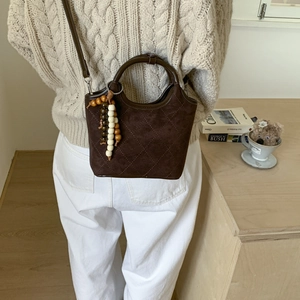 Détail d'un sac à main en daim marron foncé surpiqué avec perles en bois en décor lifestyle