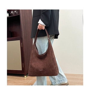 Detail of a brown suede shoulder bag with brand logo and adjustable wide strap