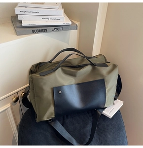 Detail of army green travel bag with black leather accents and wide handles on a blue stool