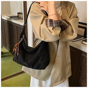 Close-up of black hobo shoulder bag with wooden bead tassel charm on a model