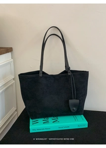 Dettaglio di borsa tote nera opaca minimalista con ciondolo su un libro vintage