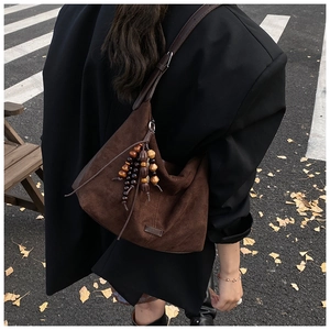 Close-up of brown suede tote bag with wooden bead tassel against autumn leaves