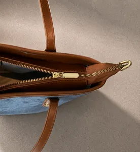 Detail view of smooth light gold metal zipper and brown leather trim on the tote bag