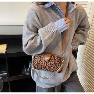 Detail showing leopard print texture, round metal clasp and silver chain strap on crossbody bag