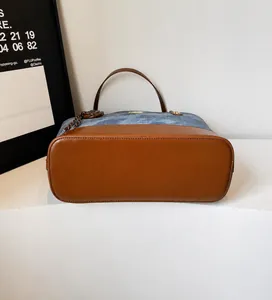 Detail of blue denim tote bag with brown leather base and metallic brand nameplate