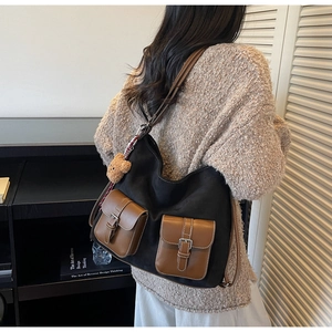 Dettaglio della borsa in tela nera con tasche in pelle marrone e ciondolo orsetto di peluche