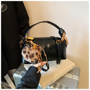 Close-up of black glossy leather cylinder bag with leopard heart charm and metal ring handle