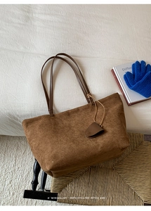 Dettaglio di una borsa tote in pelle scamosciata marrone con sottili tracolle e ciondolo sobrio
