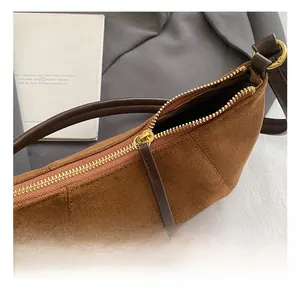 Dettaglio della cerniera dorata e del materiale scamosciato marrone della borsa a tracolla