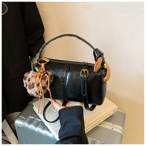 Detail of black faux leather handbag with gold metal rings and leopard print pompom charm