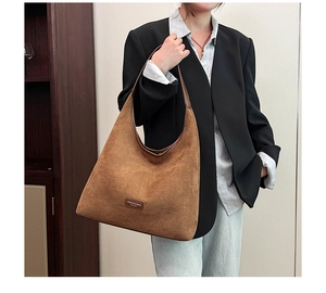 Close-up of brown suede hobo bag featuring leather handle and central logo patch detail