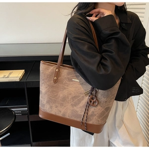 Detail of tan tote bag featuring marble texture, metal rivets, and woven rope ornament