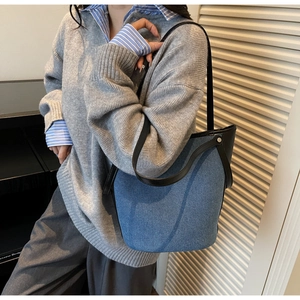 Detail view of denim and leather bucket bag with metal rivets on a shoulder strap