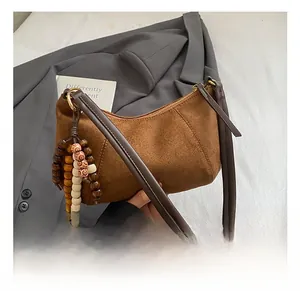 Dettaglio di borsa a mezzaluna in pelle scamosciata marrone con nappa di legno e perline