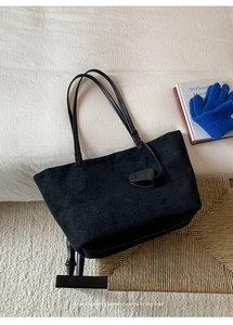 Dettaglio borsa shopper nera opaca con etichetta in pelle su sfondo sedia vintage