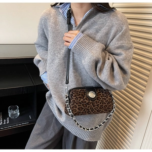 Detail showing leopard print texture, silver metal buckle and chain strap of crossbody bag