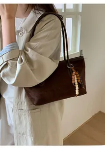 Detail of suede shoulder bag featuring a colorful beaded tassel charm and twin handles