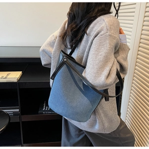 Detailed view of large denim bucket bag with black leather trim and silver metal buckle
