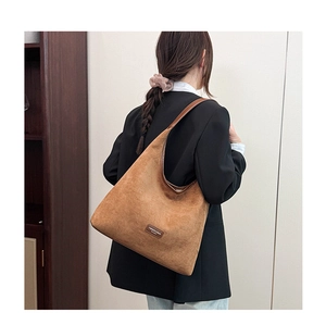 Detail of brown suede hobo bag featuring logo tag and high-quality leather shoulder strap