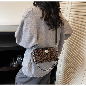 Detail of leopard print crossbody bag with silver chain worn by a model in a casual setting