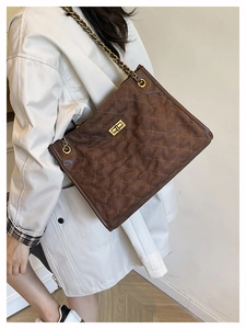 Detailed view of the brown quilted suede tote bag featuring a gold metal chain strap and lock