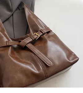Close-up of soft brown leather tote with decorative strap and brass buckle detail